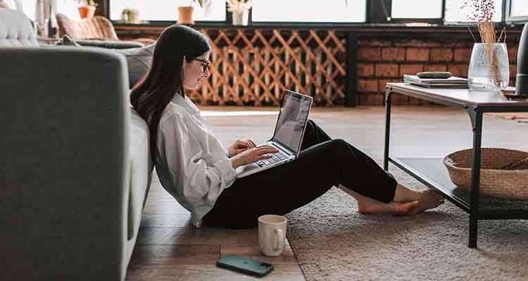 Mujer sentada en el piso y trabajando en la computadora portátil